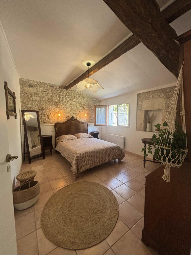 Chambre authentique avec poutres apparentes et vieilles pierre, suspension pétales, bois et rotin